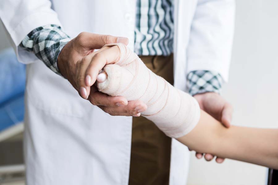 Group Accident Insurance - Woman Holding Up her Broken Arm with a Doctor Adding a Cast